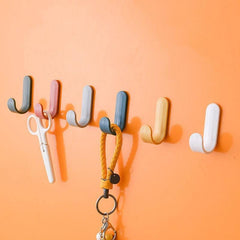 Nail free viscose adhesive hooks in various colors holding scissors and keys on an orange wall.