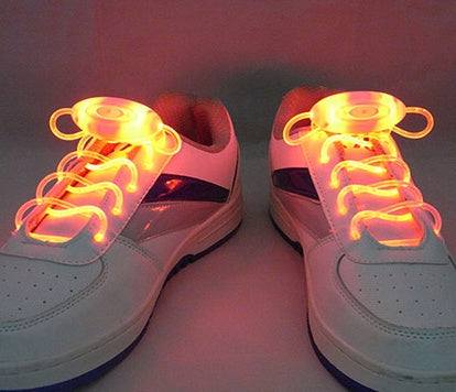 LED sport shoe laces glowing on white sneakers in a dark setting.