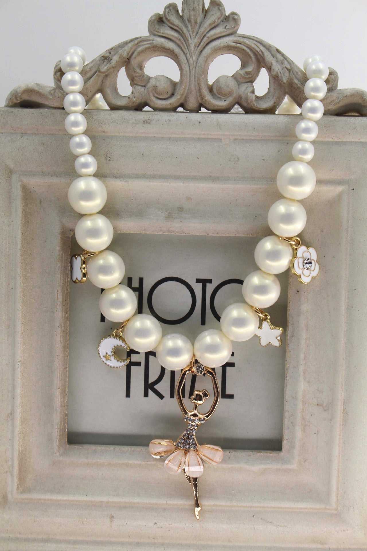 Korean jewelry accessories necklace with symphony white pearls and ballerina charm in a vintage frame background.