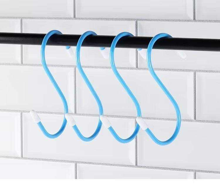 Blue rubber S-hooks hanging on a black rod in front of a tiled wall.